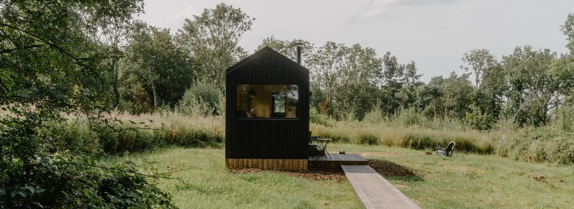 a small black cabin in a grassy area with a deck